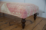 Distressed blush and antique ivory Oushak rug fragment texture on a vintage ottoman table.