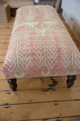 Textured blush and ivory geometric vintage Oushak rug fragment ottoman, dark wood leg.