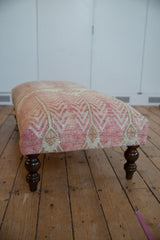 Distressed blush, ivory, tan Oushak rug fragment with geometric pattern on carved ottoman leg.