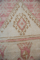 Close-up of distressed hand-knotted vintage Oushak fragment, blush pink and tan geometric patterns.