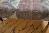 Edge of vintage rug fragment ottoman, showing distressed pile with gray, rust, and mint green geometric pattern.