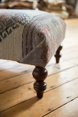 Corner of distressed Turkish rug fragment ottoman, showing woven texture and carved wooden leg.