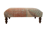Vintage Oushak rug fragment ottoman with distressed neutral patterns and carved dark wood legs.