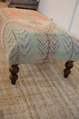 Ottoman table corner with subdued light green geometric Oushak rug fragment and dark wood leg.