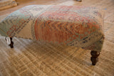 Dark brown carved wooden leg detail of the vintage Oushak rug ottoman.
