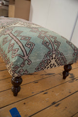 Distressed geometric turquoise and lavender rug fragment and dark wooden leg.