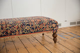 Persian Rug Ottoman, side view: navy, blush, ivory floral pattern, curved wooden leg.
