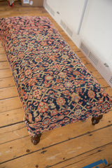 Vintage Persian rug ottoman side view: navy, blush, ivory intricate pattern with a curved wooden leg.