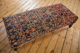 Hand-knotted vintage Persian rug fragment on ottoman with navy, blush, and ivory geometric pattern.