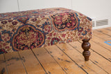 Antique Kerman rug fragment ottoman, beige, ruby, cobalt floral design with aged texture.