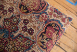 Detailed view of antique Kerman rug fragment, showcasing worn beige, cobalt blue, and crimson floral motifs.
