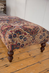Antique Kerman rug fragment, beige, red, blue floral design, and turned wooden leg.