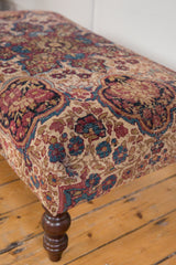 Corner detail of antique Kerman rug fragment ottoman; beige, ruby, cobalt floral pattern.