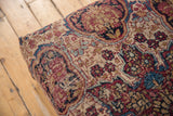 Ornate antique Kerman rug fragment featuring beige, red, blue motifs, and visible foundation wear.