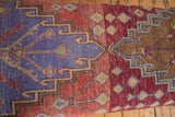 Detail of vintage Turkish Oushak rug fragment featuring geometric patterns in raspberry, lavender, and brown with natural wear.