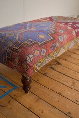 Vintage Oushak rug fragment ottoman corner, showcasing vibrant geometric patterns and turned leg.