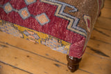 Corner of vintage Oushak rug fragment on ottoman with raspberry red, golden yellow, mint green geometric pattern.
