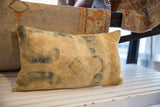 Antique Chinese rug fragment pillow displaying faded blue-green motifs on a soft tan base.