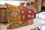 Textured edge of vintage Oushak rug fragment pillow, revealing yellow, blue, and maroon geometric patterns.