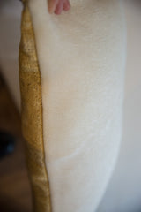 Pillow's side detail, showing woven cream fabric and textured mustard gold rug fragment.