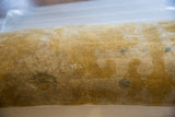 Aged gold pile with subtle blue pattern on a rolled antique Chinese rug fragment.