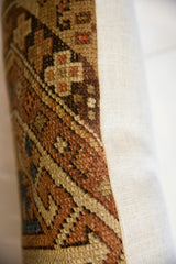 Pile of antique Caucasian rug fragment pillow, earthy geometric patterns contrasting cream backing.