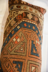 Textured geometric pattern of antique Caucasian rug fragment pillow in rust, blue, and beige.