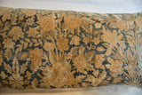 Textured close-up of antique Kerman rug fragment with muted gold, deep blue florals.