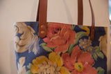 Close-up of vintage floral fabric tote bag with colorful blooms and leather strap.