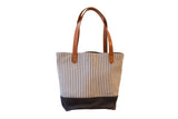 Vintage ticking stripe market tote bag with dark base and brown leather handles.