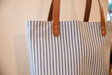 Navy ticking stripe pattern on tote bag fabric, with brown leather straps and rivets.