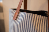 Vintage ticking stripe market tote bag's top edge, brown leather handle, and copper rivets.