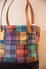 Sturdy brown leather handle secured with two brass rivets to the multicolored plaid tote.