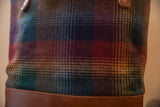 Plaid fabric tote detail showing blue, green, red, and yellow gradient with stitched brown leather.
