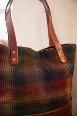 Vintage plaid tote bag fabric texture in red, green, gold, with leather strap rivets.