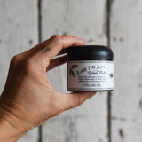 A hand holding the small jar of Bartram Wood Balm by Peg & Awl.