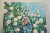 Woman's hand reaching for a pale pink rose amidst lush green foliage.