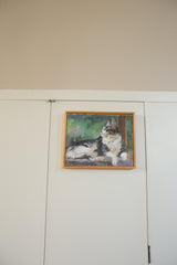 Impressionistic portrait of a reclining gray and white cat, framed in simple natural wood.