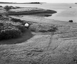 A small white boat sits on a grassy hill overlooking the calm coastal waters of Maine.