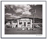 A classic black and white photograph of the Mora Valley Oil Company, a vintage gas station in rural New Mexico.
