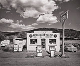 The vintage Mora Valley Oil Company building and pumps under a dramatic, cloudy New Mexico sky.