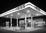 High-contrast black and white photograph of a brightly illuminated Hess Gas Station at night.