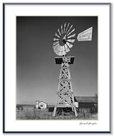 Framed black and white photograph of an Aeromotor windmill in a rural New Mexico landscape with a church.