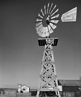 Black and white photo of an Aeromotor windmill and small church in the New Mexico landscape.