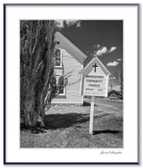 A black and white photograph of Bridgeport Community Church, showing its white siding and hand-painted sign.