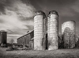 The textured, domed tops of two weathered silos stand out against a dramatic, cloudy sky.