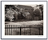 A black and white photograph of a rustic wooden barn in Pennsylvania behind a dark picket fence.