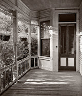 Weathered wooden side porch with peeling paint on the railing, captured in black and white.