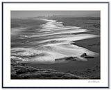 Black and white photograph of a moody shoreline with waves blurred by a long time exposure.
