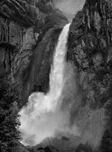 A close view of Yosemite Falls' powerful cascade in black and white against dark granite cliffs.